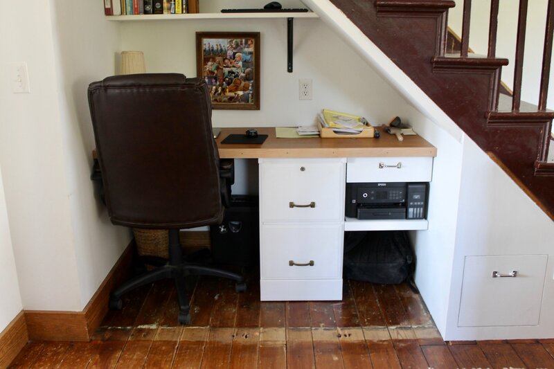 Compact under-stair office setup with built-in shelving, task lighting, and efficient use of vertical space in a small nook