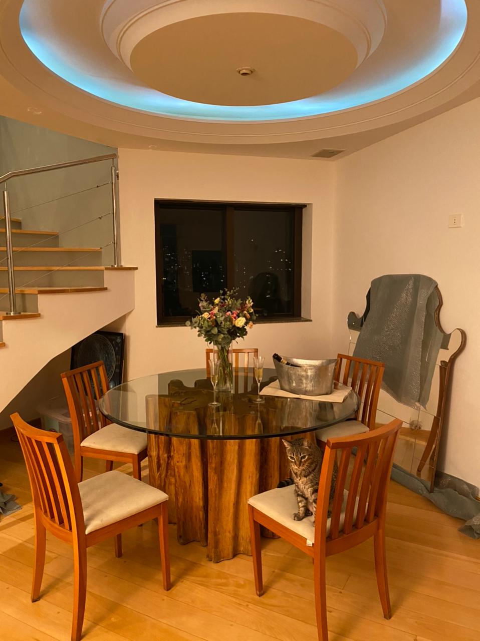 Mesa de jantar redonda com tampo de vidro e base de madeira maciça, acompanhada de 4 cadeiras em ambiente aconchegante