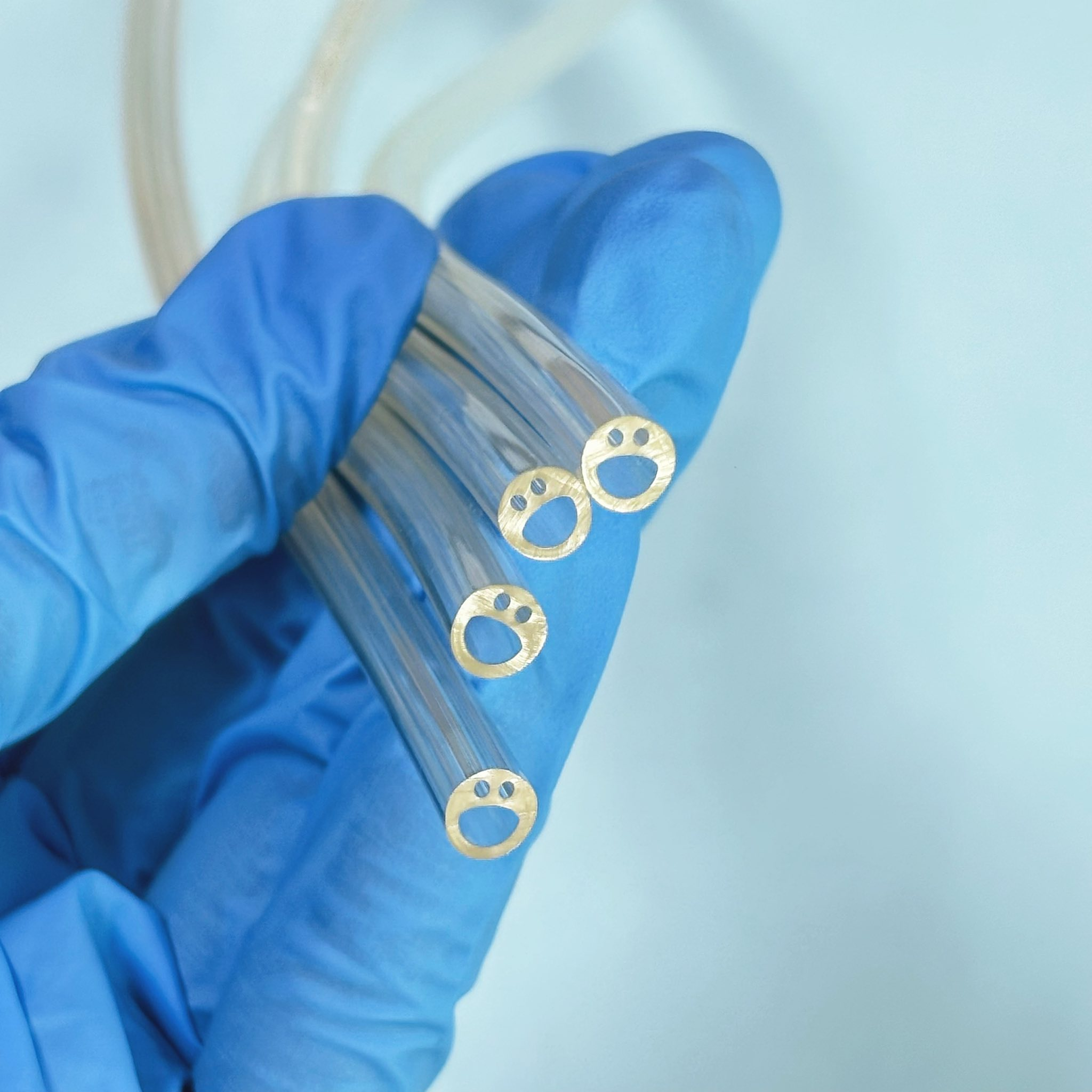 A gloved hand holding several pieces of multi-lumen medical tubing for catheters